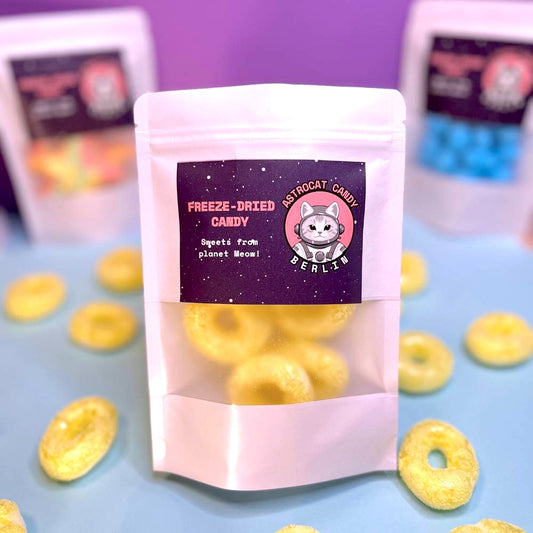 Gefriergetrocknete Bananenringe (Halal) in einem weißen Kraftpapier-Mylarbeutel – Produktvorderseite von Astrocat Candy, fotografiert vor neutralem Hintergrund.
