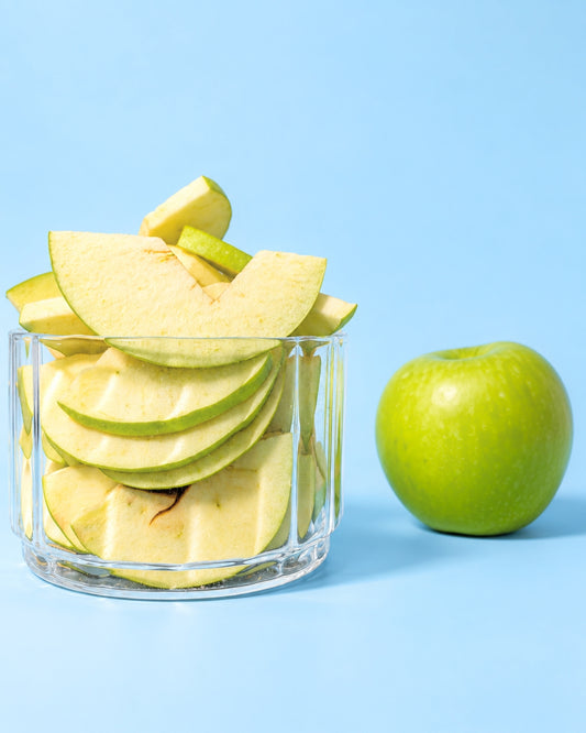 Gefriergetrocknete saure Apfelscheiben im Glas mit frischem Apfel im Hintergrund