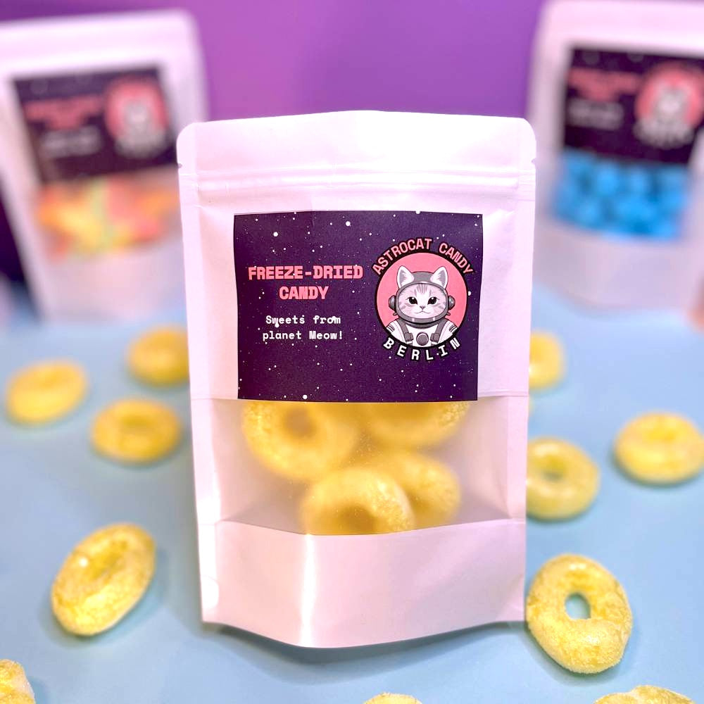 Gefriergetrocknete Bananenringe (Halal) in einem weißen Kraftpapier-Mylarbeutel – Produktvorderseite von Astrocat Candy, fotografiert vor neutralem Hintergrund.
