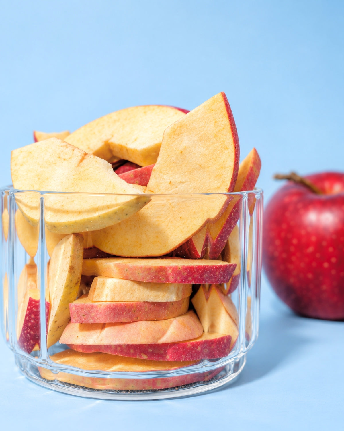 Gefriergetrocknete süße Apfelscheiben im Glas mit frischem Apfel im Hintergrund