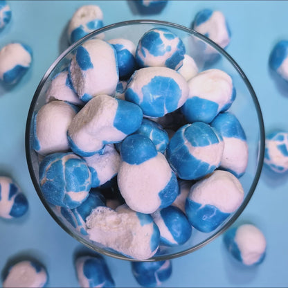 Gefriergetrocknete Krachmacher Blue fallen von oben in einen Glasbehälter – Draufsicht auf die blaue Fruchtgummi-Mischung von Astrocat Candy.