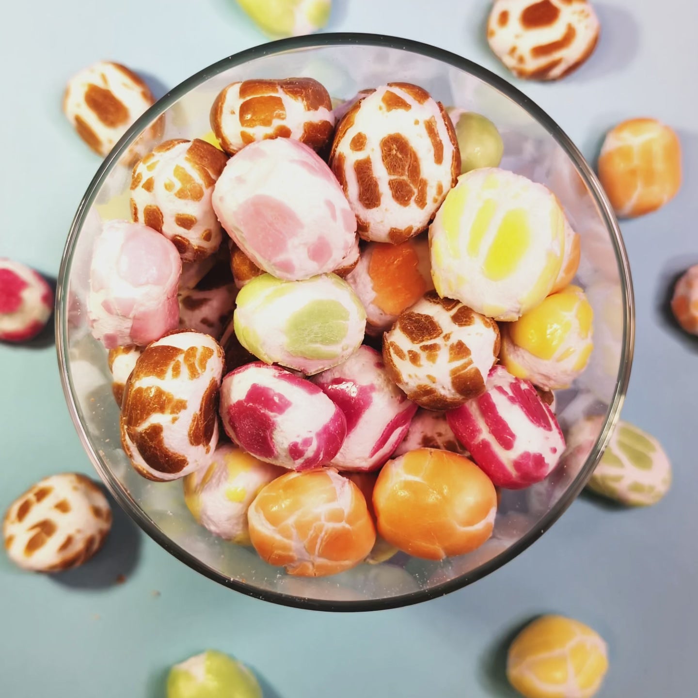 Einige gefriergetrocknete Krachmacher Frucht-Süßigkeiten fallen von oben in einen Glasbehälter, der bereits mit farbenfrohem Krachmacher-Mix gefüllt ist. Draufsicht. Produkt von Astrocat Candy.
